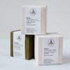 Three boxes in pale pink, pale grey and forest green are in a stack.