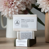A stack of soap boxes in pale pink, pale grey and forest green with bellybands