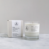 A clear glass jar candle in front of a pale grey candle box
